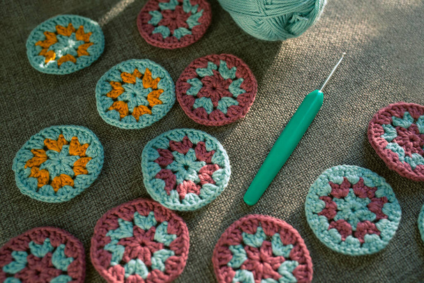 Closeup of crochet circles and a hook with part view of cotton skein on grey textured fabric in hard light and shadows. Crochet round motifs making concept. - Photo, Image