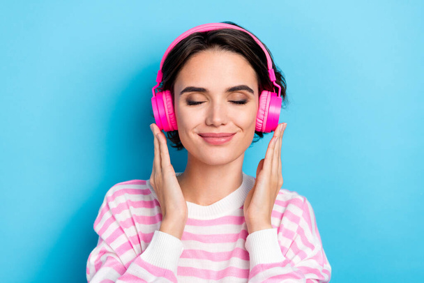 Close-up photo of adorable girl with closed eyes listening favorite music in pink headset isolated on blue color background. - Foto, Imagem