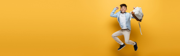 Excited asian schoolchild holding backpack and jumping on yellow background, banner  - Foto, afbeelding