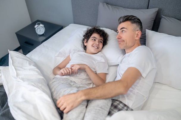 Dobré ráno. Otec a syn si ráno povídají v posteli a vypadají vesele. - Fotografie, Obrázek