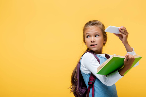 Schoolkid holding smartphone and book isolated on yellow  - Fotoğraf, Görsel