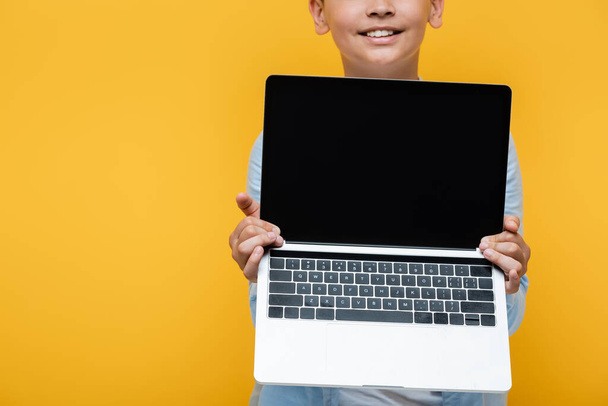 Cropped view of positive preteen schoolboy holding laptop isolated on yellow  - Fotó, kép