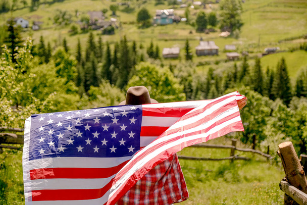 Молодая женщина стоит на горе и держит флаг США в руках. Празднование Дня независимости США. Молодая американка подняла флаг США в руках. - Фото, изображение