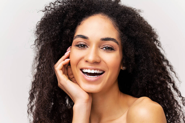 Magnificent african-american woman isolated on white background looking at the camera and smiling toothy. Well-looking young multiracial lady with naked shoulders laughing playfully. Selfcare concept - Foto, immagini
