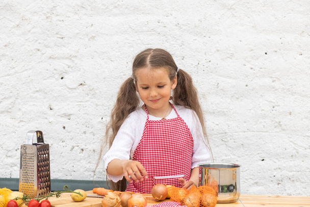 Glückliches kleines Mädchen im Kochkostüm hilft beim Kneten des Teigs, ein Kind lächelt, kocht nach einem Rezept, ein Mädchen hilft beim Kochen für Mama, Porträt und Entwicklung eines Kindes. - Foto, Bild