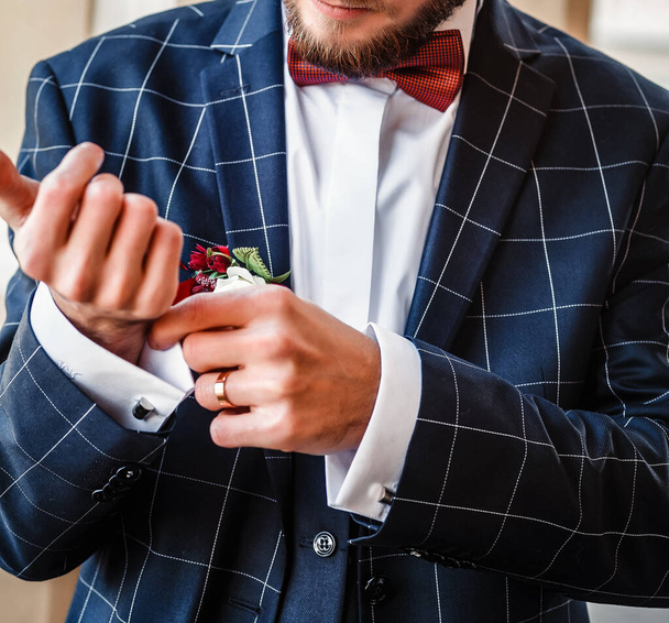 Blurred wedding background. a young man in a plaid suit straightens his shirt cuffs. the groom in a blue jacket straightens the cufflink on the sleeve of a white shirt. Wedding preparations. selective focus. - Fotografie, Obrázek