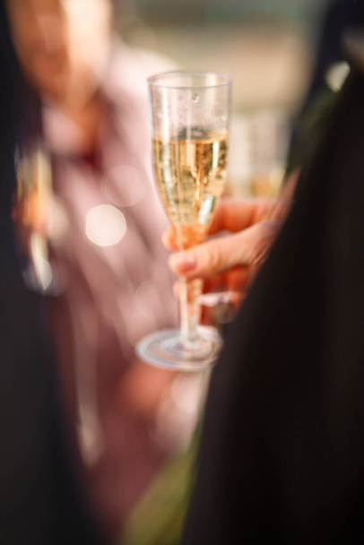 New Year's blurred festive background with a man's hand with a glass of champagne and bokeh from fireworks. wedding champagne party. the groom in a suit holds a glass of champagne in his hand. blurry - Фото, изображение