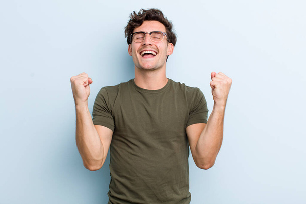 young handsome man looking extremely happy and surprised, celebrating success, shouting and jumping - 写真・画像