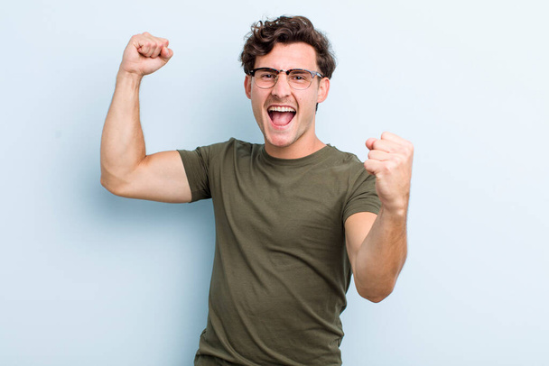 young handsome man shouting triumphantly, looking like excited, happy and surprised winner, celebrating - Foto, Imagen