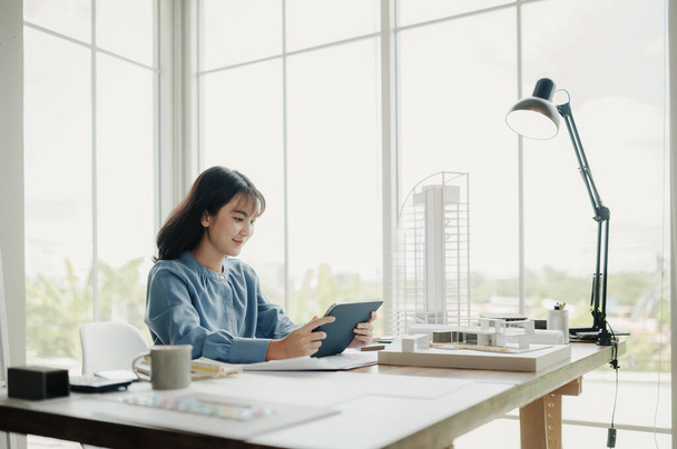 Selective focus, Asian female architect or engineer Drawing the design of the building's interior using a tablet. Asian female architect or engineer Sit and analyze, design projects in the office. - Foto, afbeelding