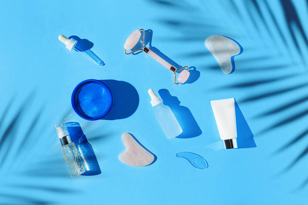 Cosmetic facial kit for home skin care and spa. Collagen eye patches, face roller and gua sha massagers, bottles of essential oil and serum on blue pastel background. Natural treatment concept. Top view. Flat lay - Photo, Image