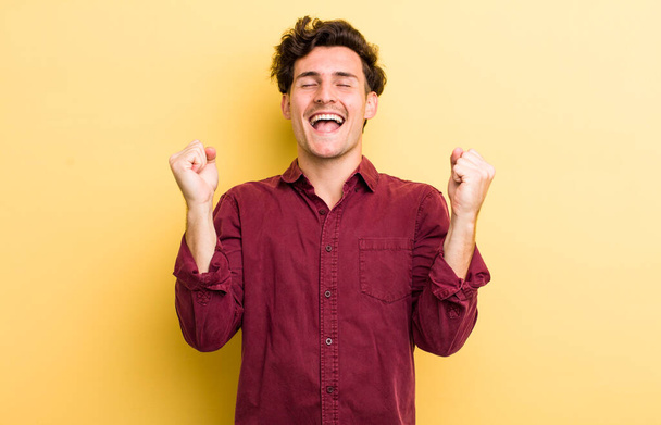 young handsome man looking extremely happy and surprised, celebrating success, shouting and jumping - Fotoğraf, Görsel