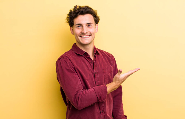 young handsome man smiling cheerfully, feeling happy and showing a concept in copy space with palm of hand - Фото, зображення