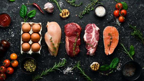 keto diet concept. Raw ingredients for zero carb or low carb diet - rib eye, salmon steak, pork, egg. Top view. On a black stone background. - Foto, Imagen