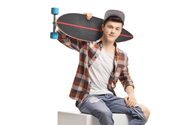 Teenager sitting and holding a longboard isolated on white background - Foto, afbeelding