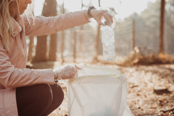 Przycięta aktywistka pomaga oczyścić las z odpadów plastikowych, śmieci. Biorę butelki do torby. Globalny ekologiczny problem recyklingu, ochrony planety przed zanieczyszczeniem. Rozwój zrównoważony - Zdjęcie, obraz