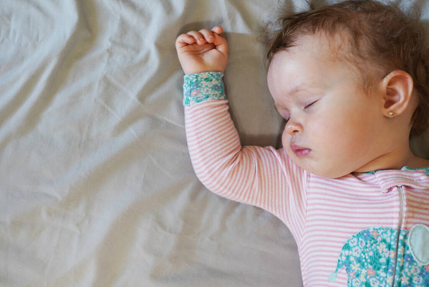 Bebé tranquilo acostado en una cama mientras duerme sobre fondo gris - Foto, Imagen