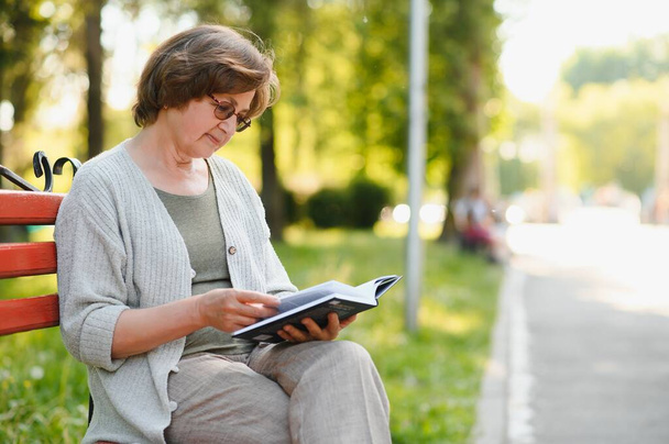 Retired woman reading a book on the bench. - Foto, afbeelding
