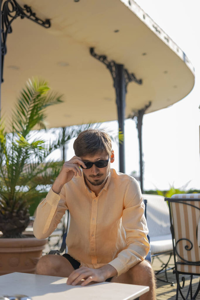Ein europäisch aussehender Mann mit orangefarbenem Hemd und Sonnenbrille. Ein tropisches Land im heißen Sommer.  - Foto, Bild