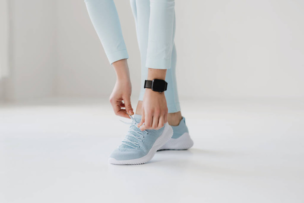 Low section of sporty woman tying shoelace on white background. Copy space. - Φωτογραφία, εικόνα