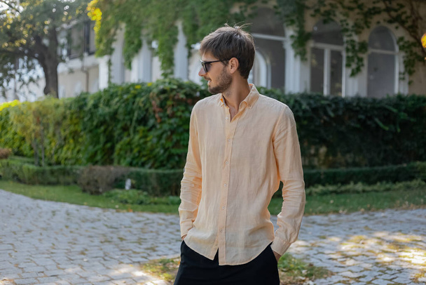 Turuncu gömlek ve güneş gözlüğü takan Avrupalı bir adam. Sıcak yaz mevsiminde tropikal bir ülke.  - Fotoğraf, Görsel