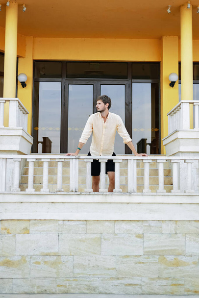 Um homem de aparência europeia com uma camisa laranja e óculos de sol. Um país tropical no verão quente. Escadaria de mármore branco. - Foto, Imagem