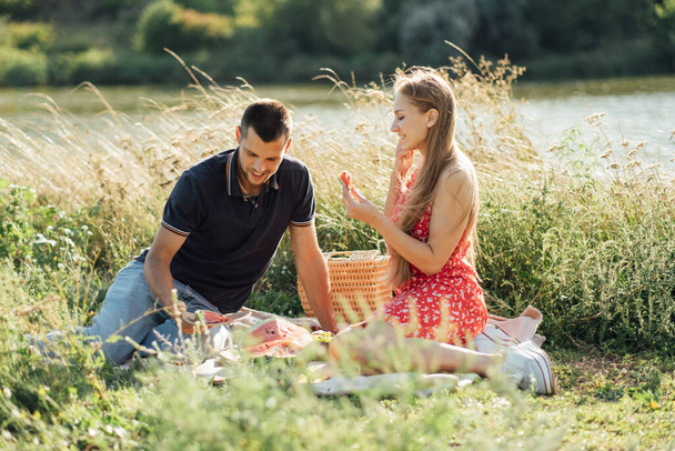 Young happy loving couple embracing and having fun together outdoors. Young couple in love on summer picnic with watermelon. - Photo, image