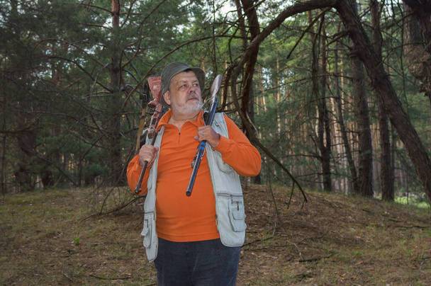 Portrait de ranger ukrainien âgé sévère avec deux fusils debout dans la forêt de pins sombres avec la volonté de défendre son pays  - Photo, image
