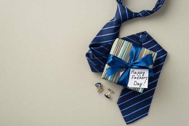 Concepto del Día del Padre. Foto vista superior de la elegante caja de regalo con lazo de cinta de seda y corbata azul postal y gemelos sobre fondo gris pastel aislado - Foto, Imagen