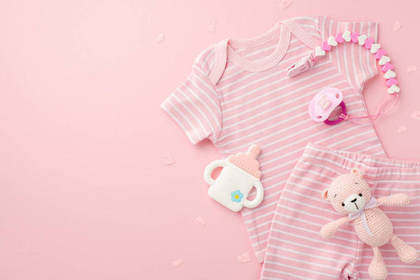 Концепция детских принадлежностей. Вид сверху фото розовые рубашки шорты ребенка фиктивная бутылка в форме цепи троса и вязаные игрушки медведя на изолированном светло-розовом фоне с пустым пространством - Фото, изображение