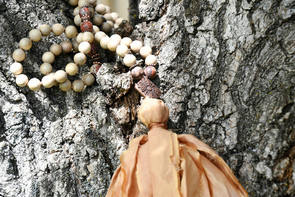 Zbliżenie wizerunek mala naszyjnik z drewnianymi koralikami i wstążką frędzle spoczywające na gałęzi drzewa.   - Zdjęcie, obraz