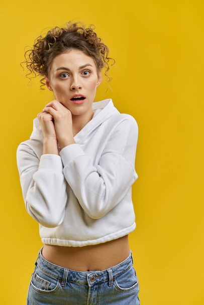 Beautiful woman with curly hair staring at camera with mouth agape indoors. Portrait view of pretty girl shocked or anxiously awaiting news, isolated on orange studio background. Concept of emotion. - Photo, Image