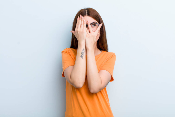young adult pretty woman covering face with hands, peeking between fingers with surprised expression and looking to the side - Foto, immagini