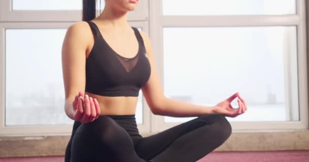 Close up of brunette girl with ponytail sitting alone with crossed legs on yoga mat, meditating. Slim, sporty female showing mudras, relaxing, breezing. Concept of yoga doing. - Záběry, video