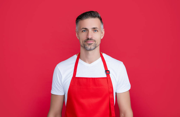 smiling mature man waiter in apron on red background. - Foto, imagen
