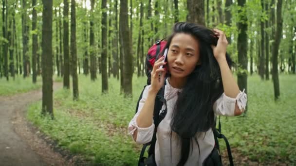 mujer asiática feliz con una mochila buscando una manera en el bosque, usando un teléfono, hablando en una videollamada, mirando un mapa. camping en verano - Imágenes, Vídeo