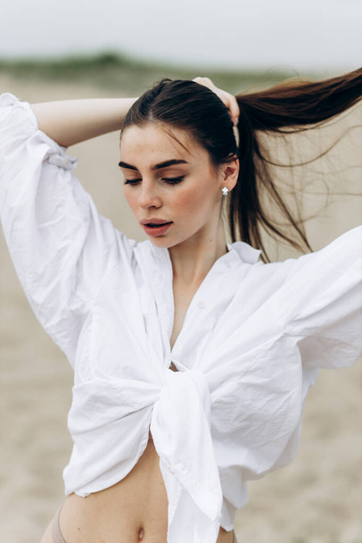 Καλοκαιρινό πορτραίτο του τρόπου ζωής της όμορφης ξανθιάς χαρούμενη νεαρή κοπέλα με μαυρισμένο σέξι σώμα σε λευκό πουκάμισο και μαγιό στέκεται στην παραλία σε τροπικό νησί παραλία με καθαρά νερά - Φωτογραφία, εικόνα