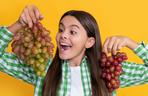 surprised teen girl with grapes bunch on yellow background. - Fotoğraf, Görsel
