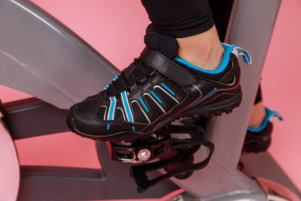 Closeup portrait of the bike simulator and women's legs in black sneakers, cardio workout. Indoor studio shot isolated on pink background. - Fotografie, Obrázek