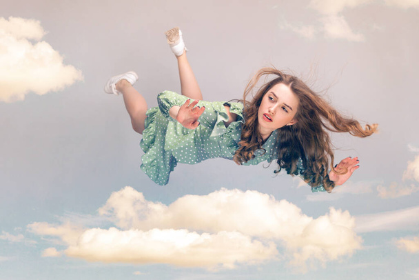 Beautiful girl levitating in mid-air, falling down and her hair messed up soaring from wind, model flying hovering with dreamy peaceful expression in sky. collage composition on day cloudy blue sky - Photo, Image