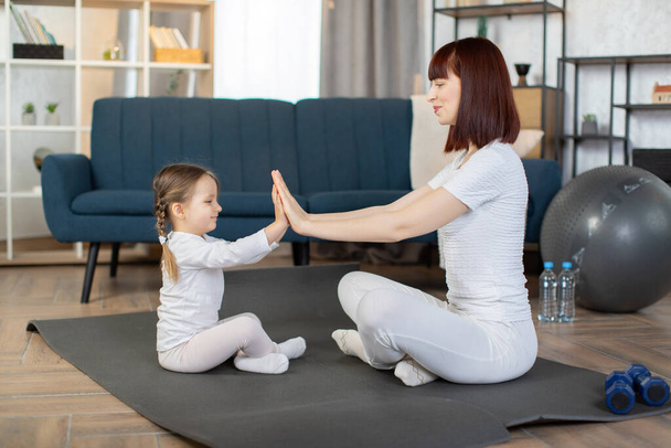 Balanced life, healthy lifestyle, family concept. Pretty Caucasian mother woman with little cute daughter, doing yoga relaxation and stretching exercise at home. - Fotoğraf, Görsel