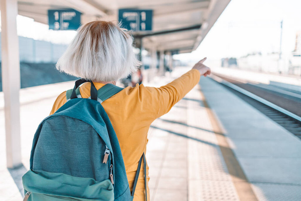 European Travel 50s fêmea com mochila de viagem mostra direção para turista longe na plataforma de trem. Foto de alta qualidade - Foto, Imagem