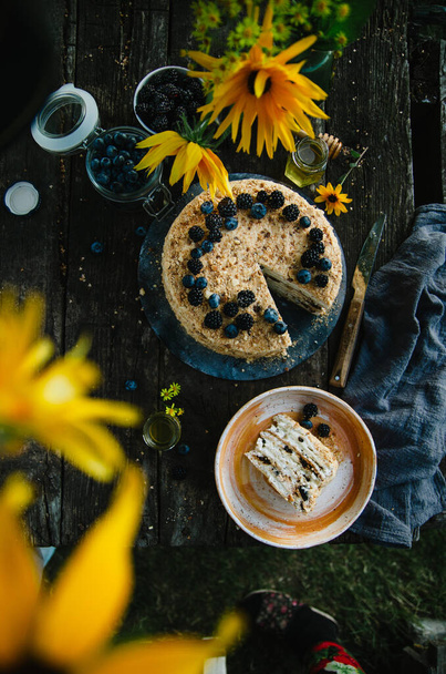 Homemade honey cake with prunes on a wooden table in nature. Cake decorated with blueberries and blackberries. Top view. Photo in rustic style. - Foto, immagini
