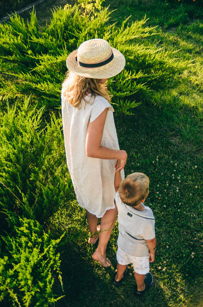 Mother walking on nature with her son. Top view from the back. Mom holds her little son by the hand. Walk on green grass. - Foto, Imagen
