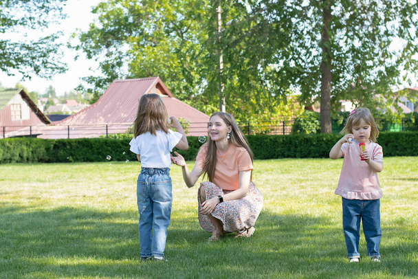 Gente. Conceito familiar. Mãe europeia e duas filhas bonitas e bonitos jogar alegremente no parque verde no verão e bolhas de sopro. Foco suave. - Foto, Imagem