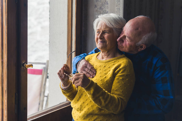 pěkný veselý senior kavkazský pár stojící u dveří okna a dívající se ven střední střílet vnitřní senioři milují koncept. Kvalitní fotografie - Fotografie, Obrázek