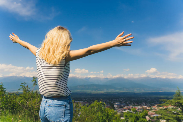 blond girl holding hands outstretched and enjoying a beautiful view of mountains and a valley. cowboy shot. High quality photo - Photo, Image