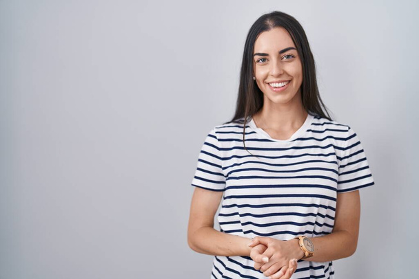 Nuori brunette nainen yllään raidallinen t paita kädet yhdessä ja ristissä sormet hymyillen rento ja iloinen. menestys ja optimistinen  - Valokuva, kuva