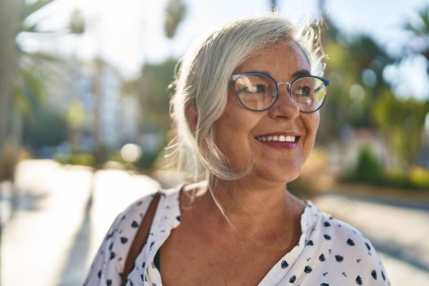 Middelbare leeftijd vrouw glimlachen zelfverzekerd staan op straat - Foto, afbeelding