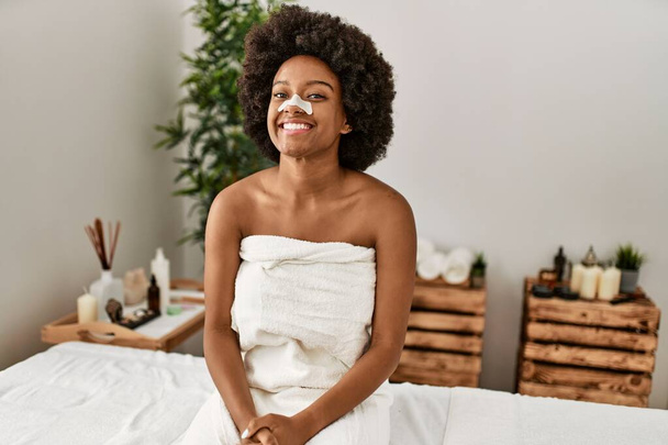 Mujer afroamericana joven sonriendo confiada usando ayuda de banda nasal en el centro de belleza - Foto, imagen